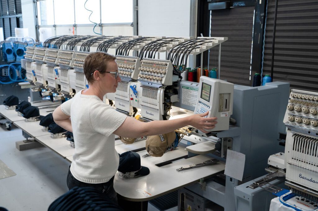 An operator runs a row of multi-head Barudan embroidery machines stitching caps in Prodigy Promos' Lindon, Utah facility