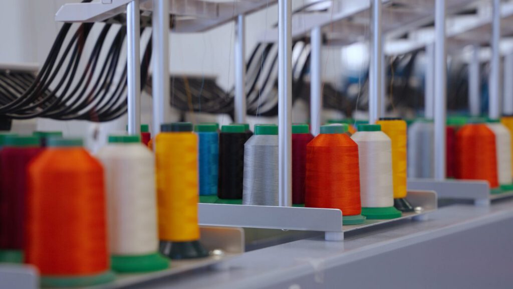 A row of colored embroidery thread cones loaded at Prodigy Promos' embroidery line in Lindon, Utah