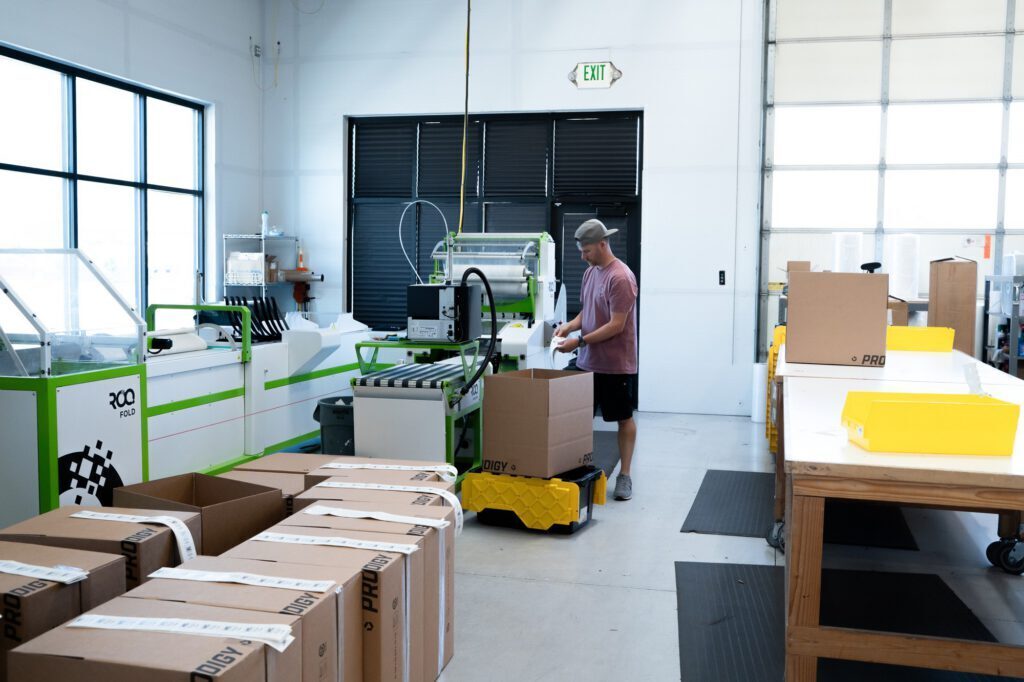 A team member packs folded, bagged apparel into Prodigy-branded boxes at the FlexONE fulfillment line in Lindon, Utah