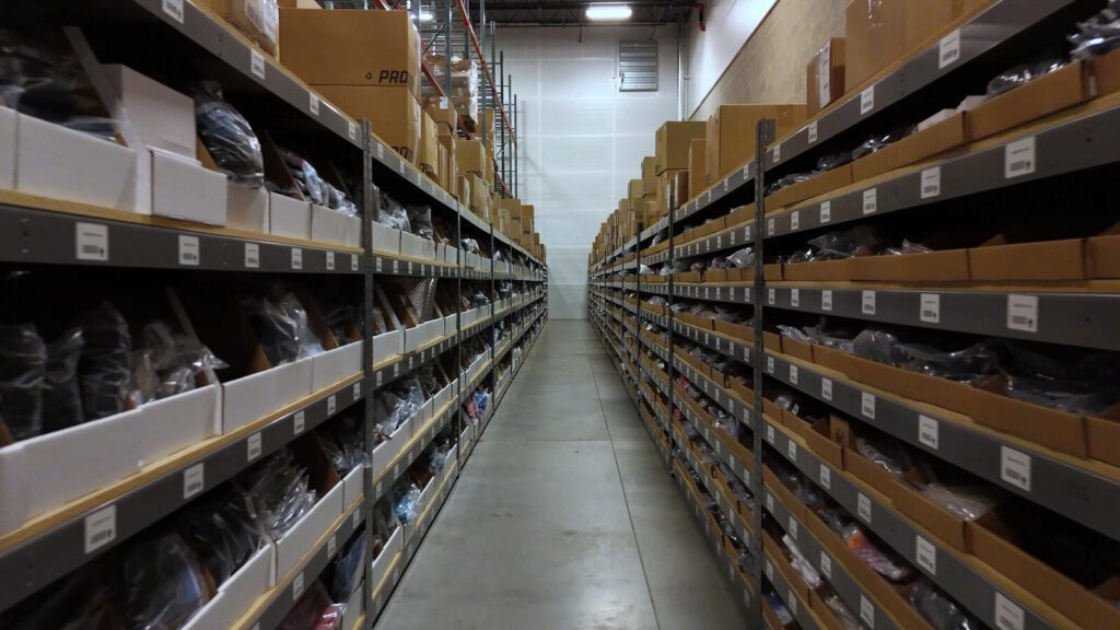 An aisle of warehouse racking stocked with bagged, boxed webstore inventory at Prodigy Promos' FlexONE fulfillment center in Lindon, Utah