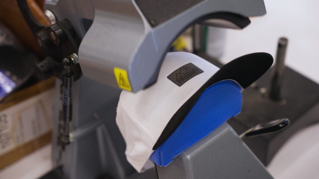 A white cap with a heat-applied Prodigy leather patch clamped in a cap heat-press at Prodigy Promos in Lindon, Utah
