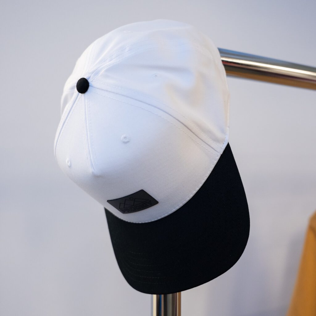 White and black cap with a debossed leather patch hanging on a display rack