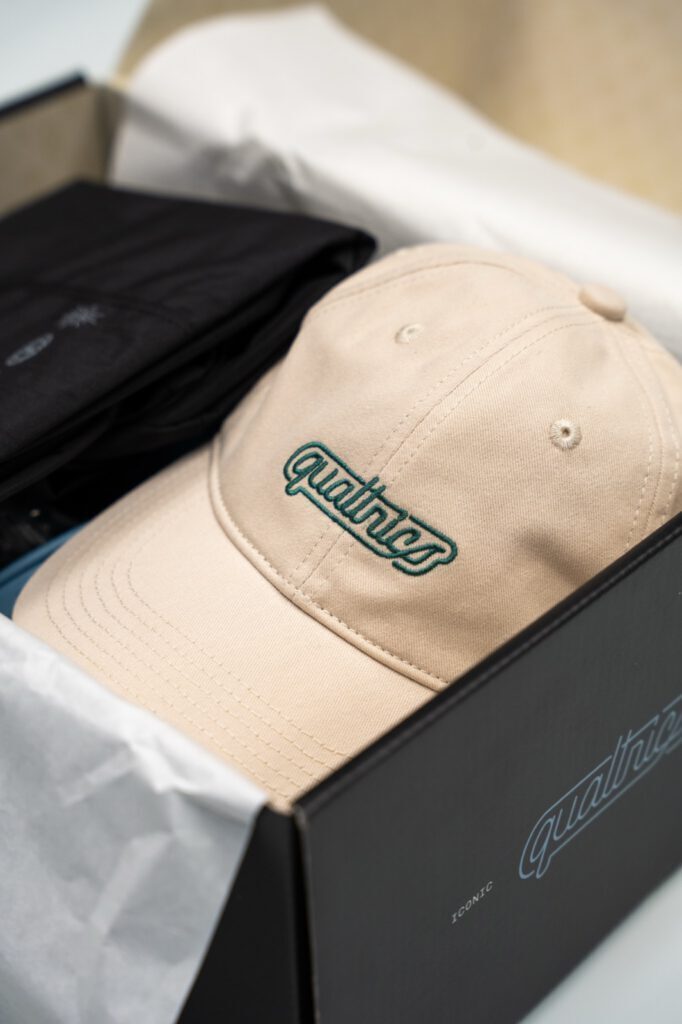 Qualtrics onboarding kit box opened to show an embroidered cap nestled in tissue paper