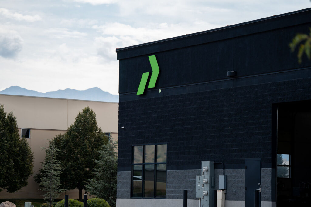 The Prodigy Promos production building in Lindon, Utah, its lime arrow mark on the black brick corner, with the Wasatch range behind