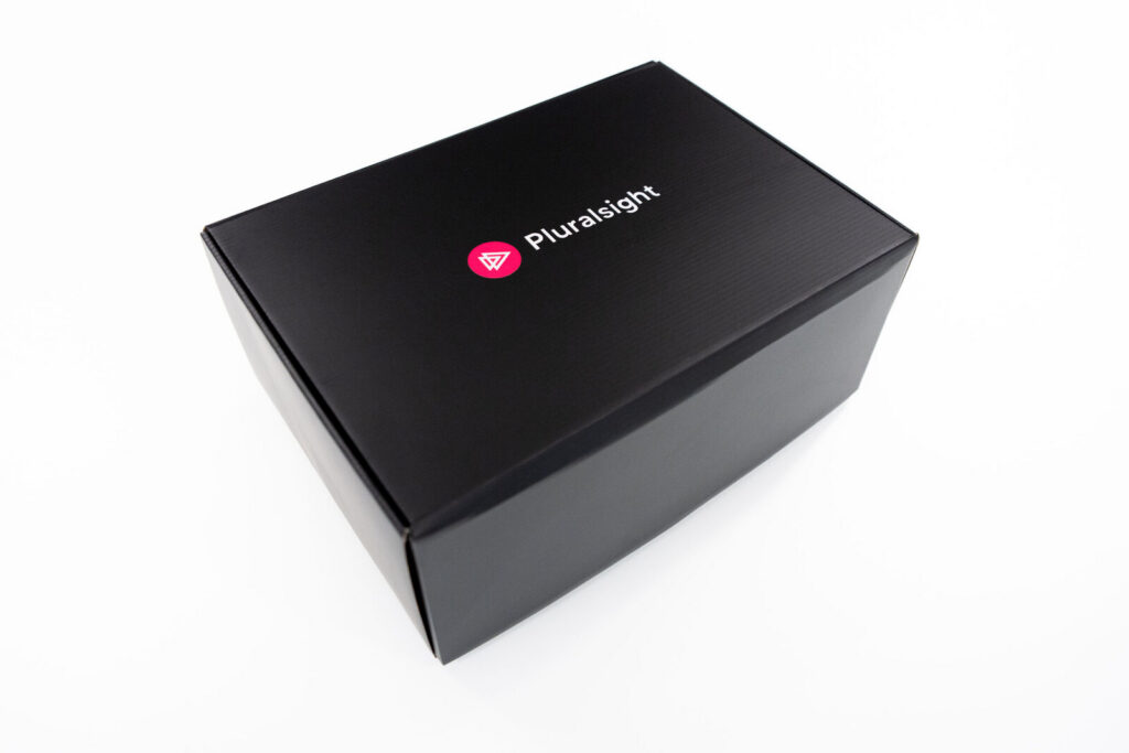 A black Pluralsight-branded onboarding kit box, closed and ready to ship
