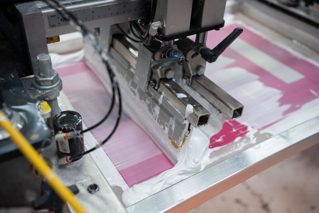 Close detail of pink screen printing ink spread across a screen on the press