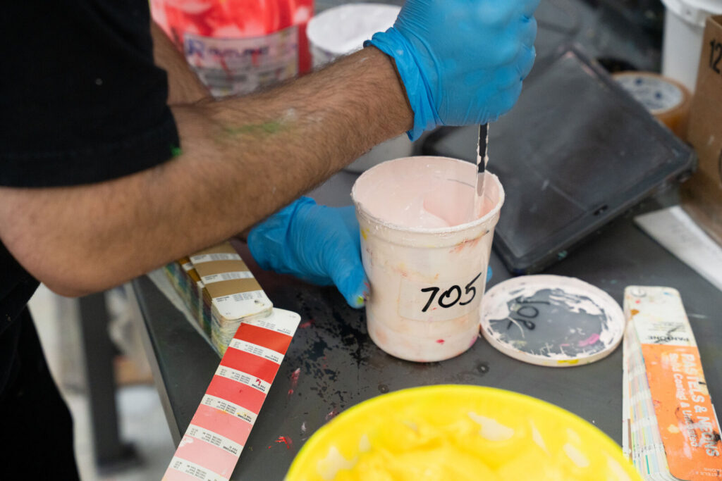 A gloved hand holding a Pantone swatch fan against freshly mixed screen printing ink
