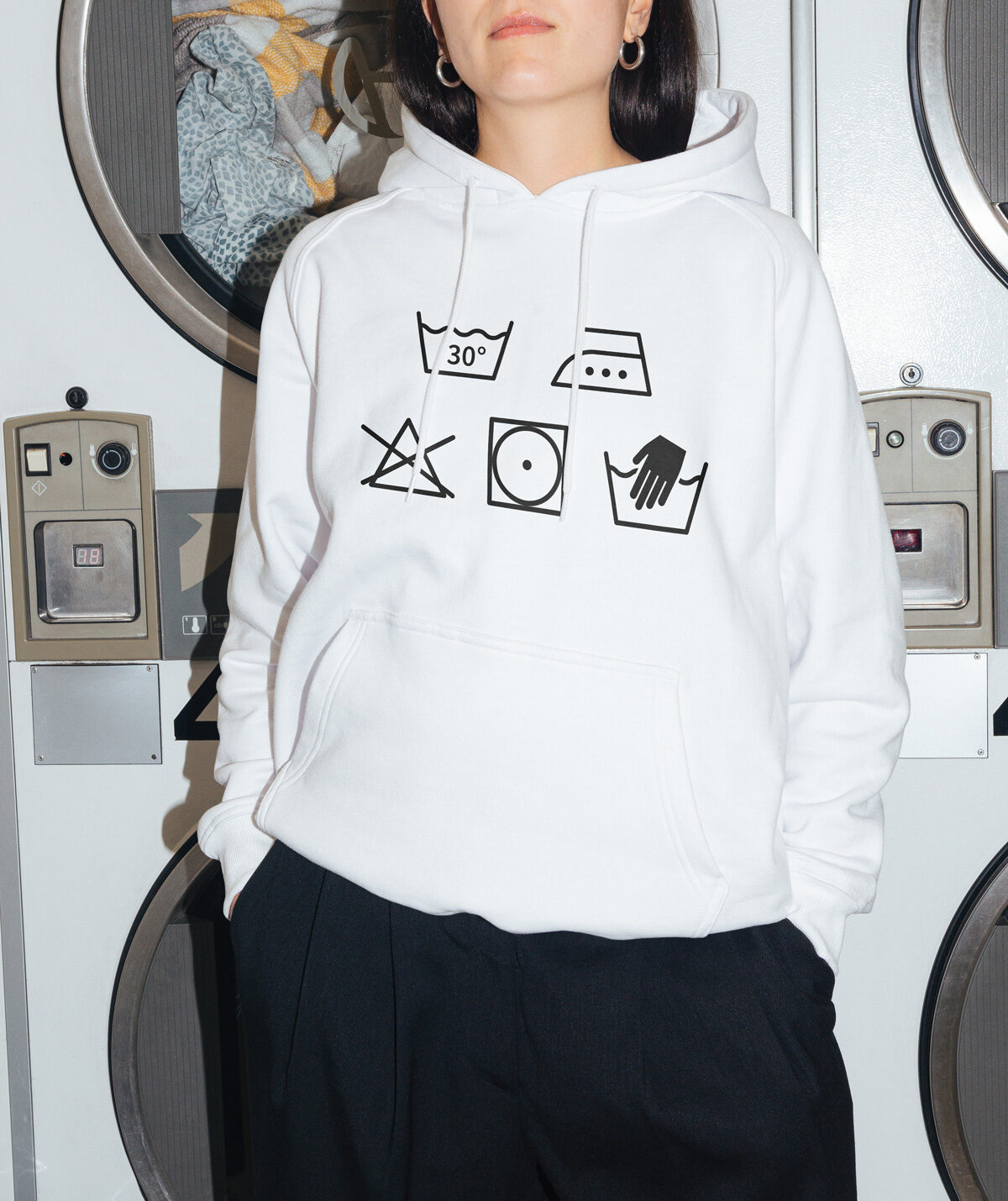 White hoodie printed with laundry care symbols in front of laundromat washing machines